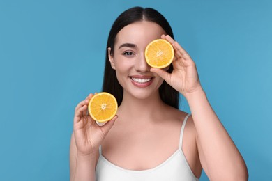 Photo of Beautiful young woman with pieces of orange on light blue background