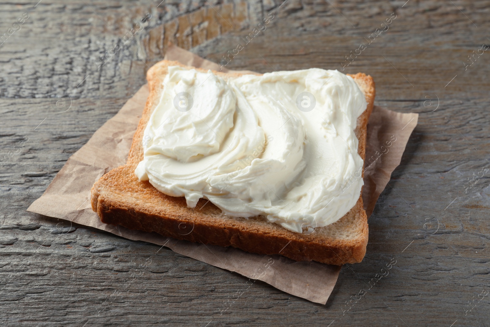 Photo of Slice of bread with tasty cream cheese on wooden table