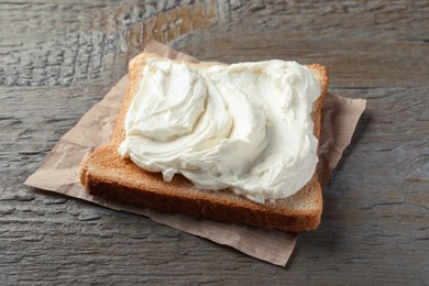 Photo of Slice of bread with tasty cream cheese on wooden table