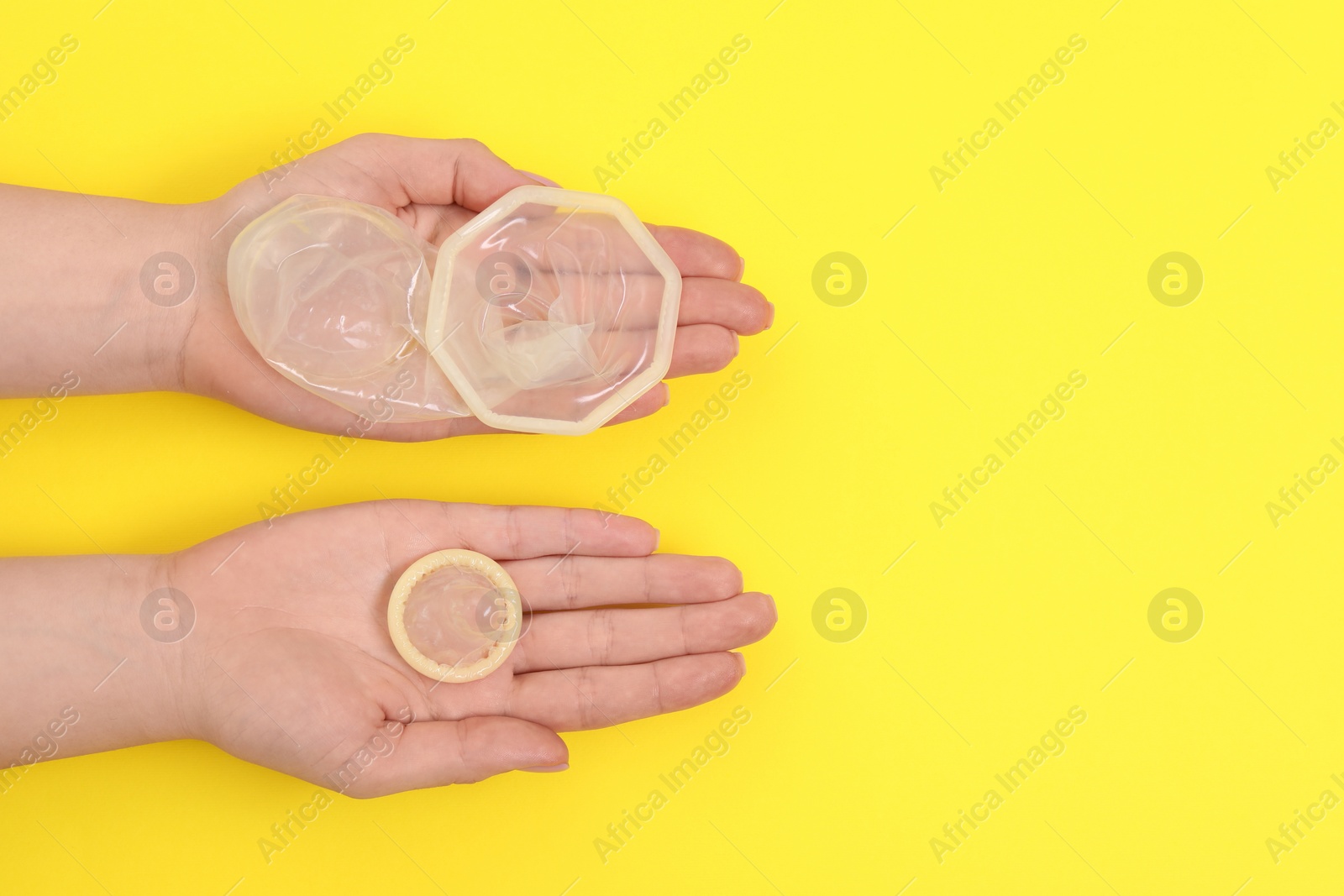 Photo of Woman with unrolled female and male condoms on yellow background, top view. Space for text