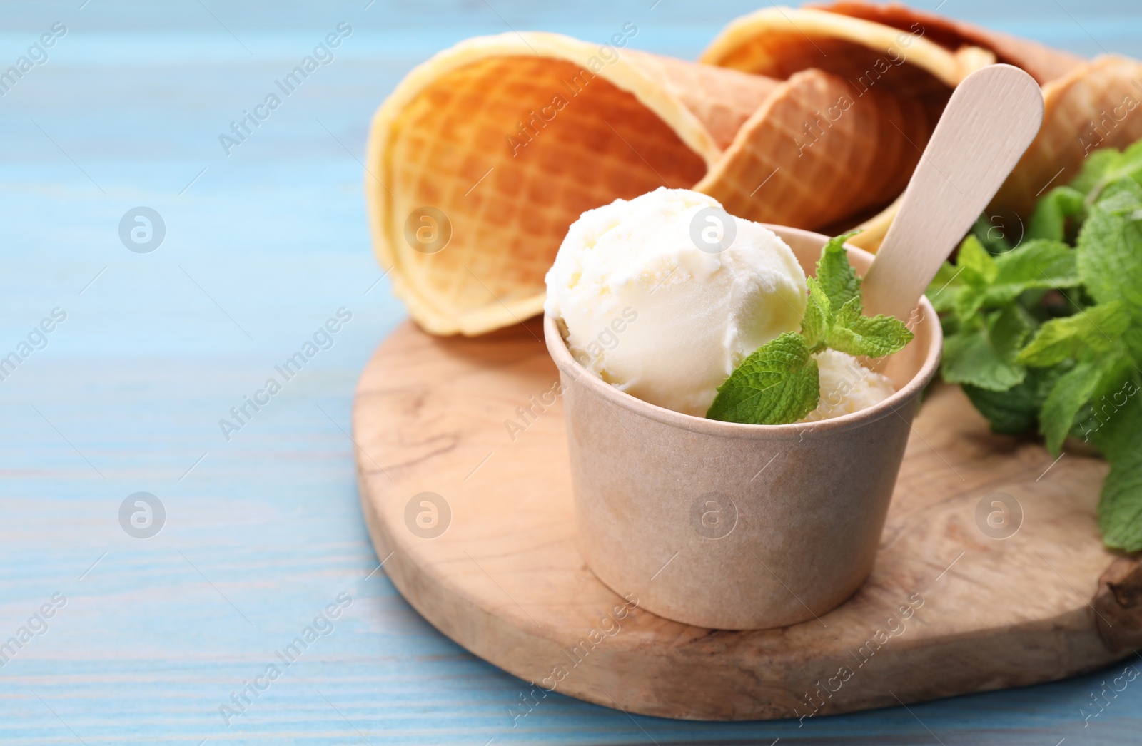 Photo of Delicious vanilla ice cream with mint in paper cup on light blue wooden table, closeup. Space for text