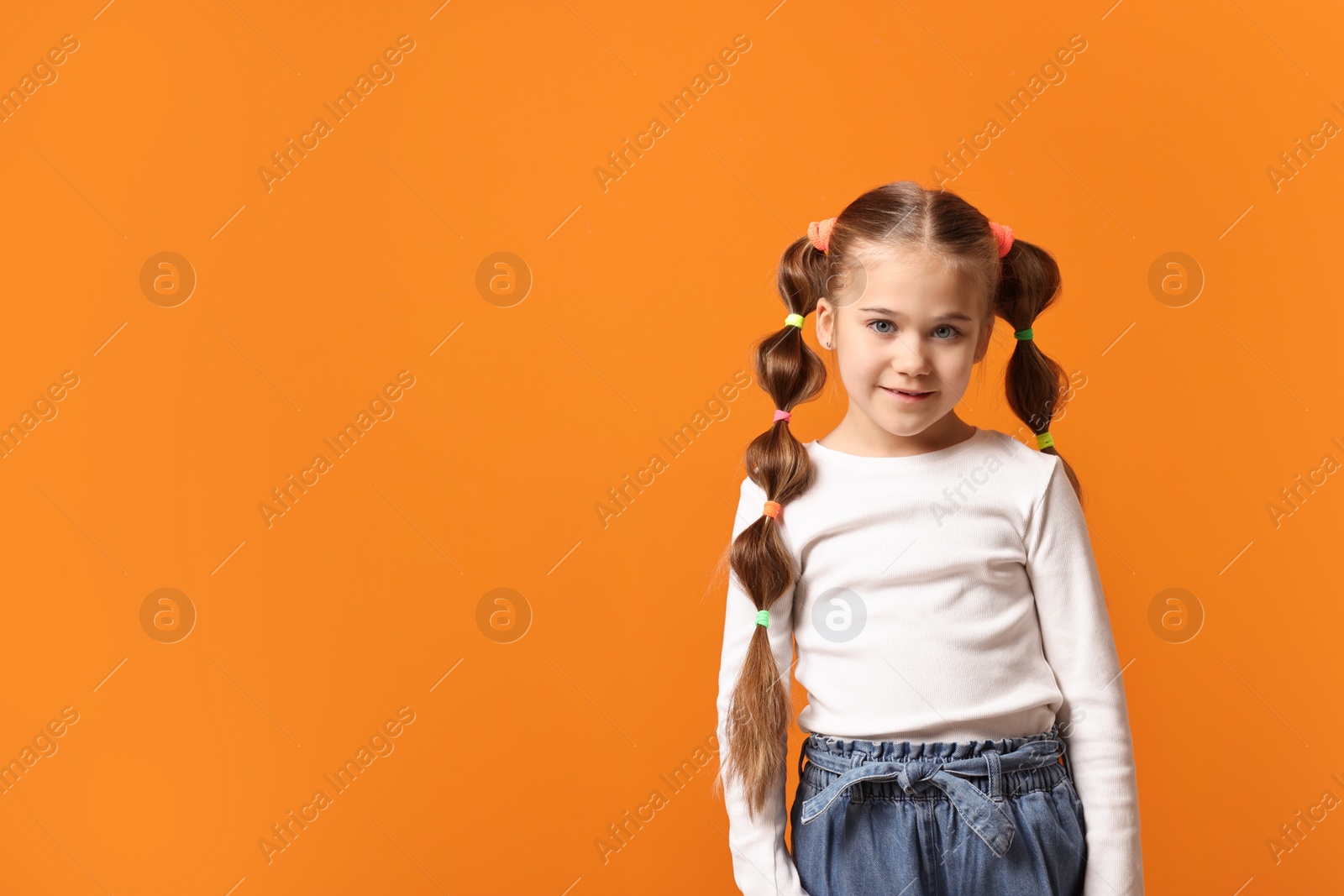 Photo of Cute little girl with beautiful hairstyle on orange background. Space for text