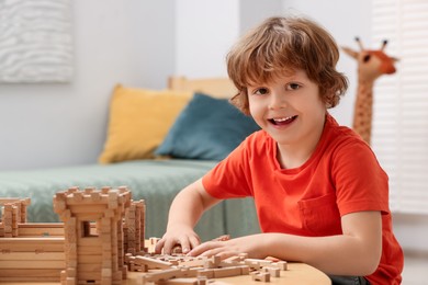 Photo of Little boy playing with wooden construction set at table in room. Child's toy