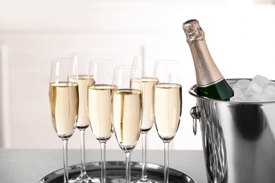 Photo of Glasses with champagne and bottle in bucket on table indoors