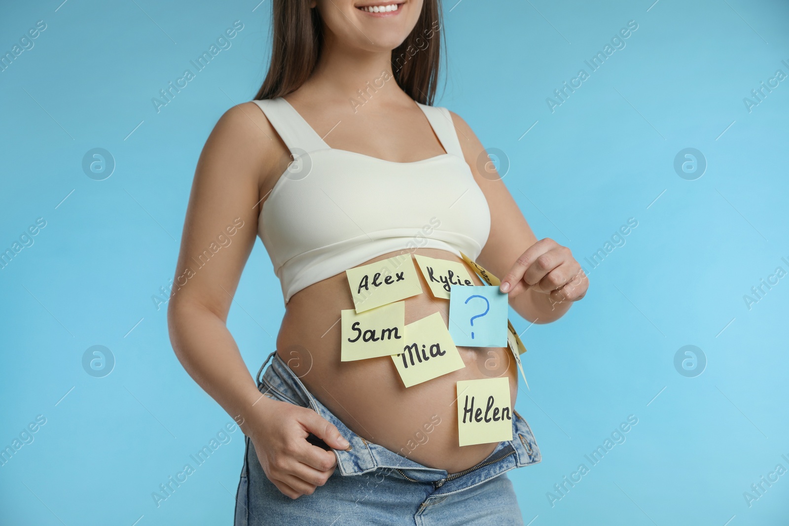 Photo of Pregnant woman with different baby names on belly against light blue background, closeup