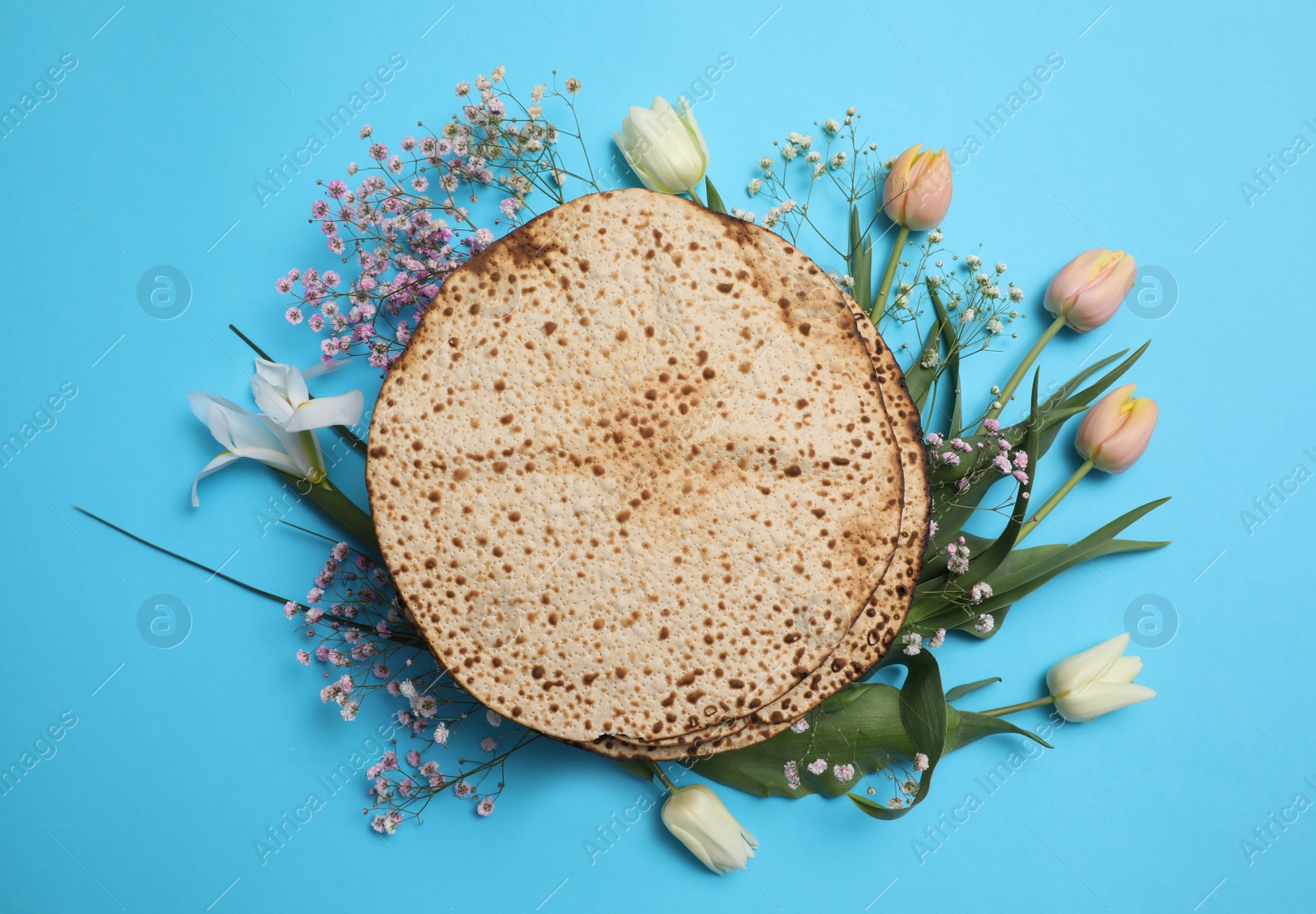 Photo of Tasty matzos and fresh flowers on light blue background, flat lay. Passover (Pesach) celebration