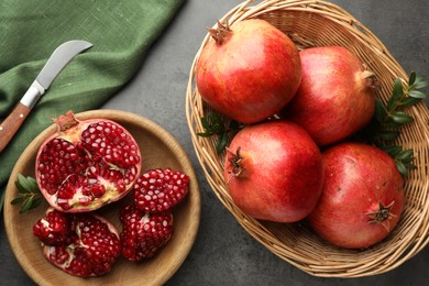 Photo of Fresh pomegranates, green leaves and knife on grey table, top view