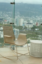 Photo of Coffee table and beige chair against picturesque landscape of city in cafe