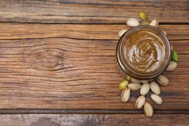 Photo of Tasty pistachio nut paste in jar on wooden table, top view. Space for text