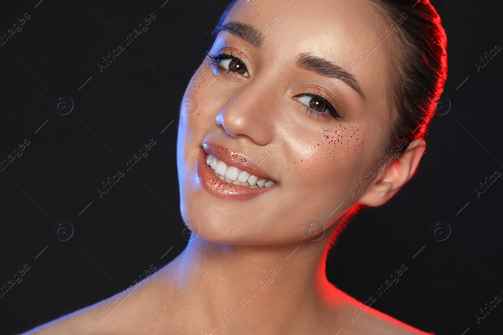 Photo of Beautiful young woman with glitter makeup on black background