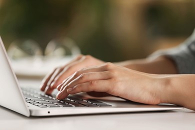 Photo of Woman working with laptop at white table indoors, closeup