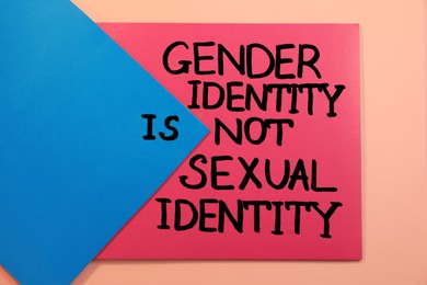 Photo of Paper with text Gender Identity Is Not Sexual Identity on pink background, top view