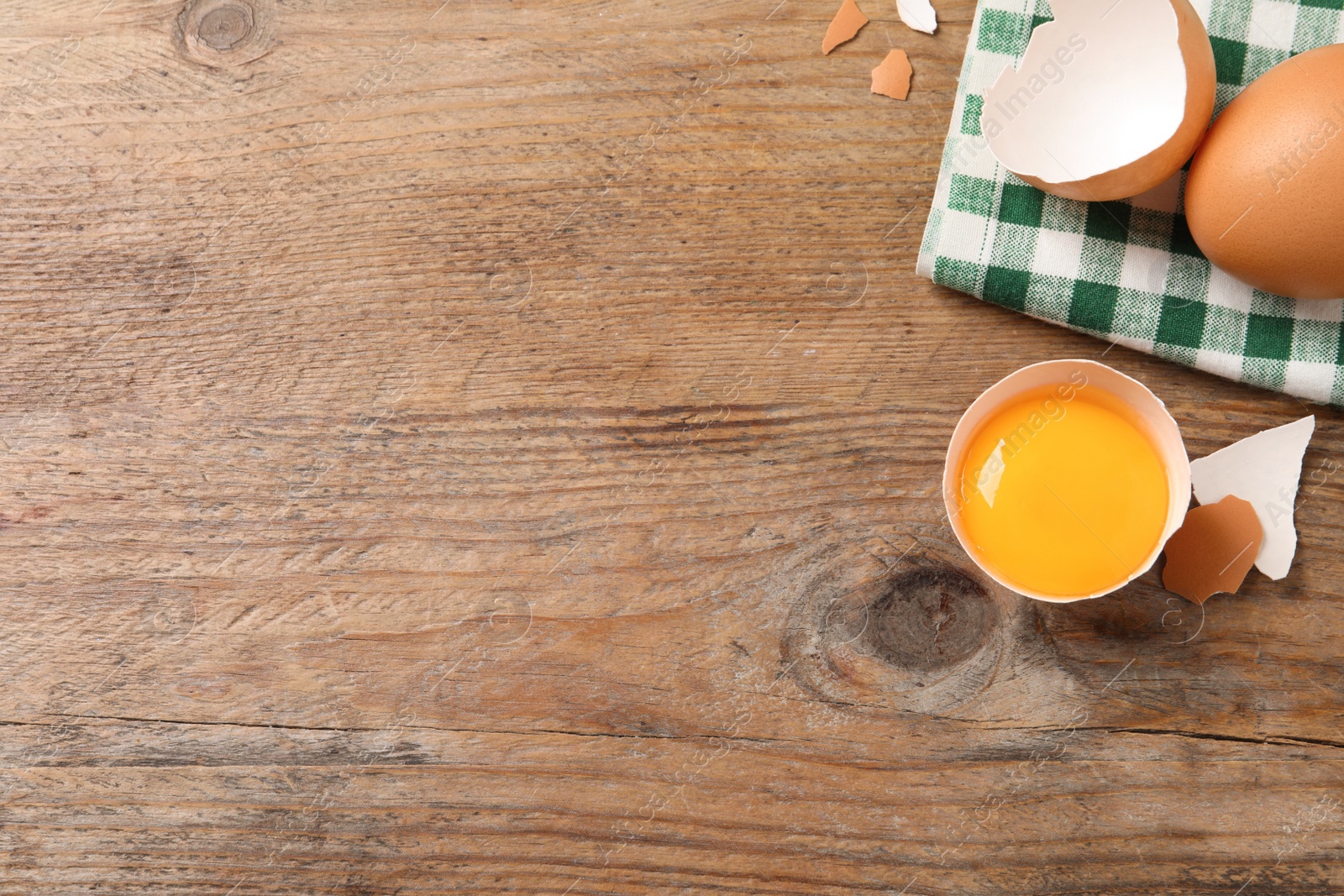 Photo of Whole and cracked chicken eggs on wooden table, flat lay. Space for text