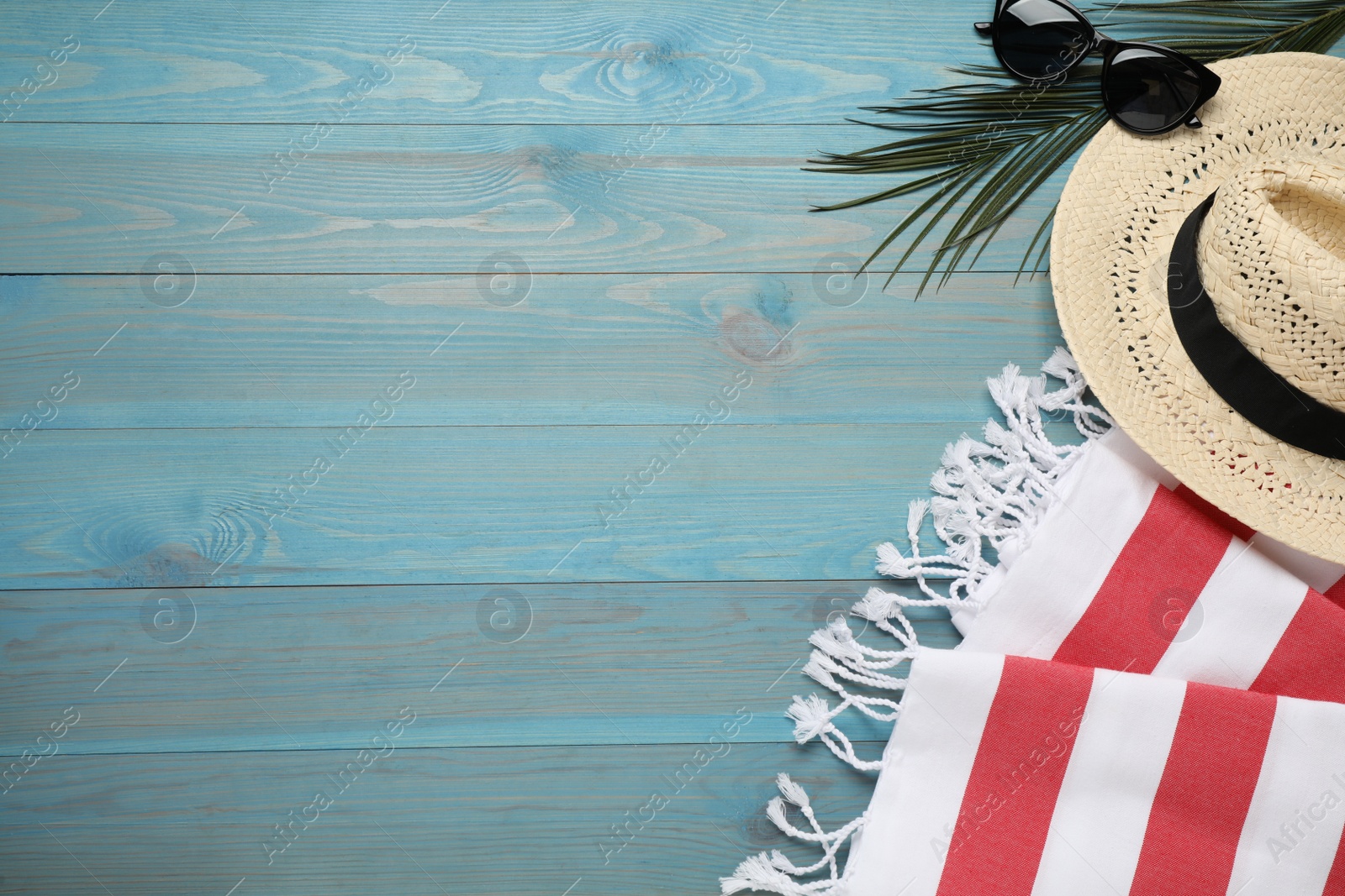 Photo of Beach towel, sunglasses and hat on light blue wooden background, flat lay. Space for text