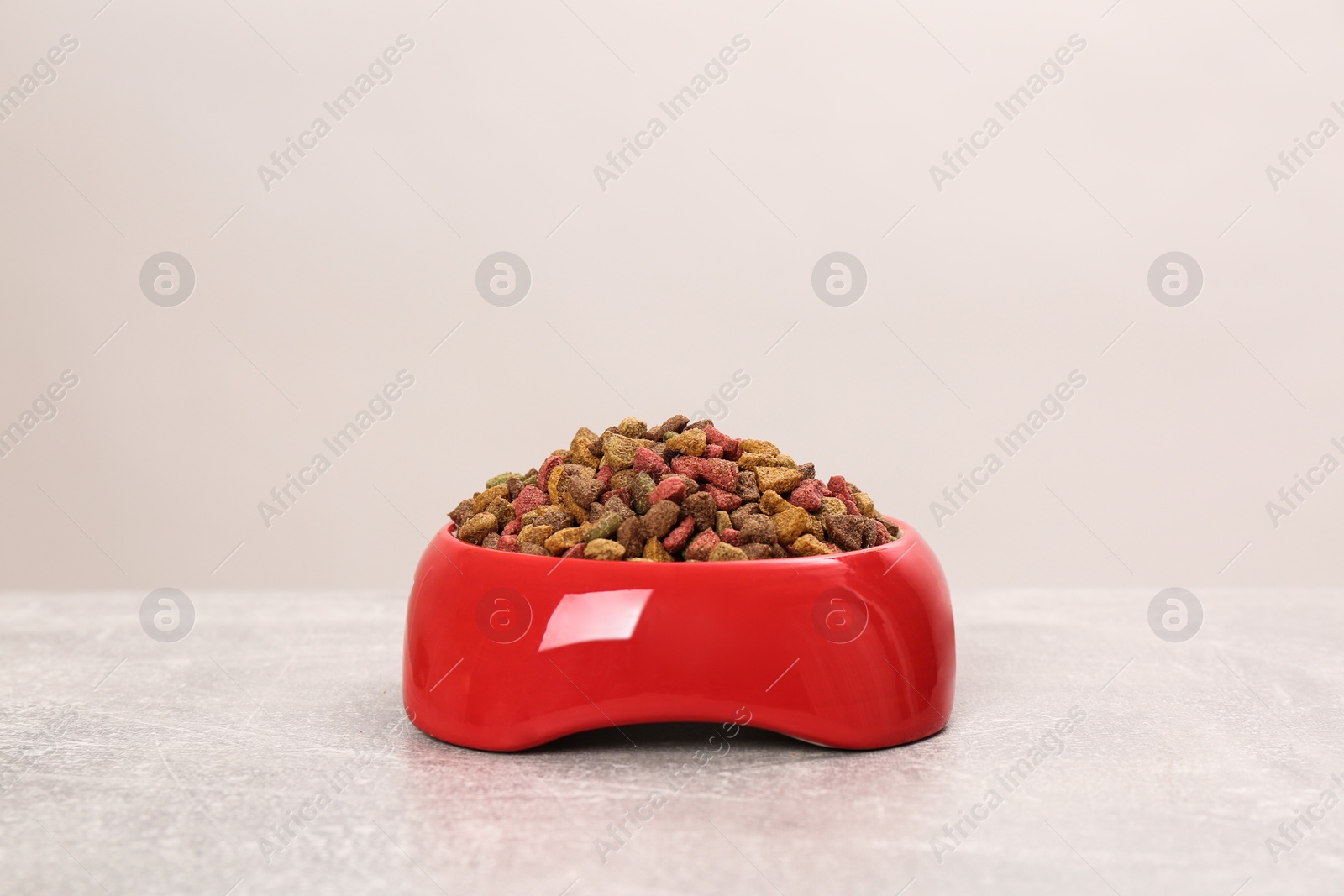 Photo of Dry cat food in red pet bowl on grey surface
