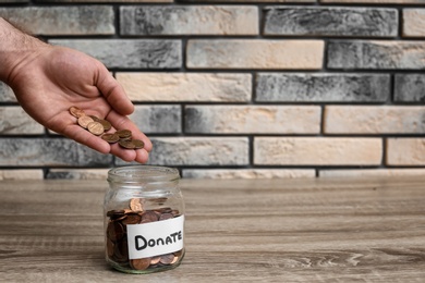 Photo of Man putting coins into donation jar on table, closeup. Space for text
