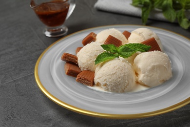 Photo of Plate of ice cream with caramel candies and mint on grey table, closeup