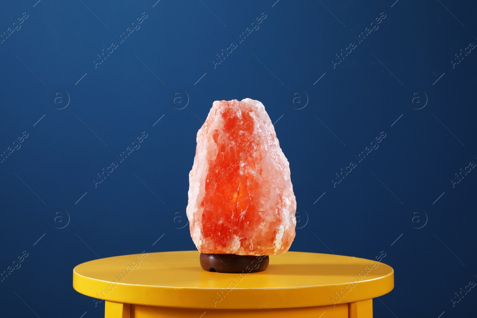 Photo of Himalayan salt lamp on yellow table against dark blue background