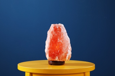 Photo of Himalayan salt lamp on yellow table against dark blue background