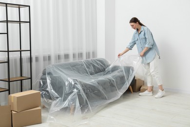Young woman covering sofa with plastic film at home