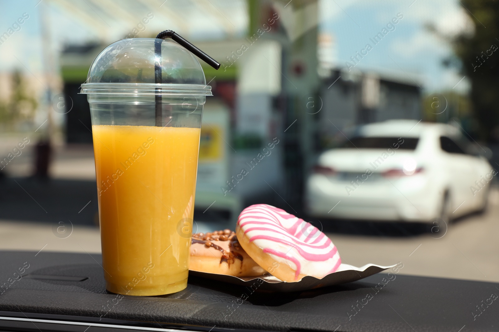 Photo of Plastic cup of juice and doughnuts on car dashboard at gas station. Space for text