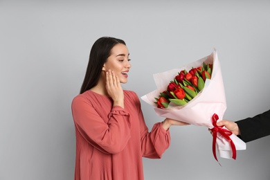 Photo of Happy woman receiving red tulip bouquet from man on light grey background. 8th of March celebration