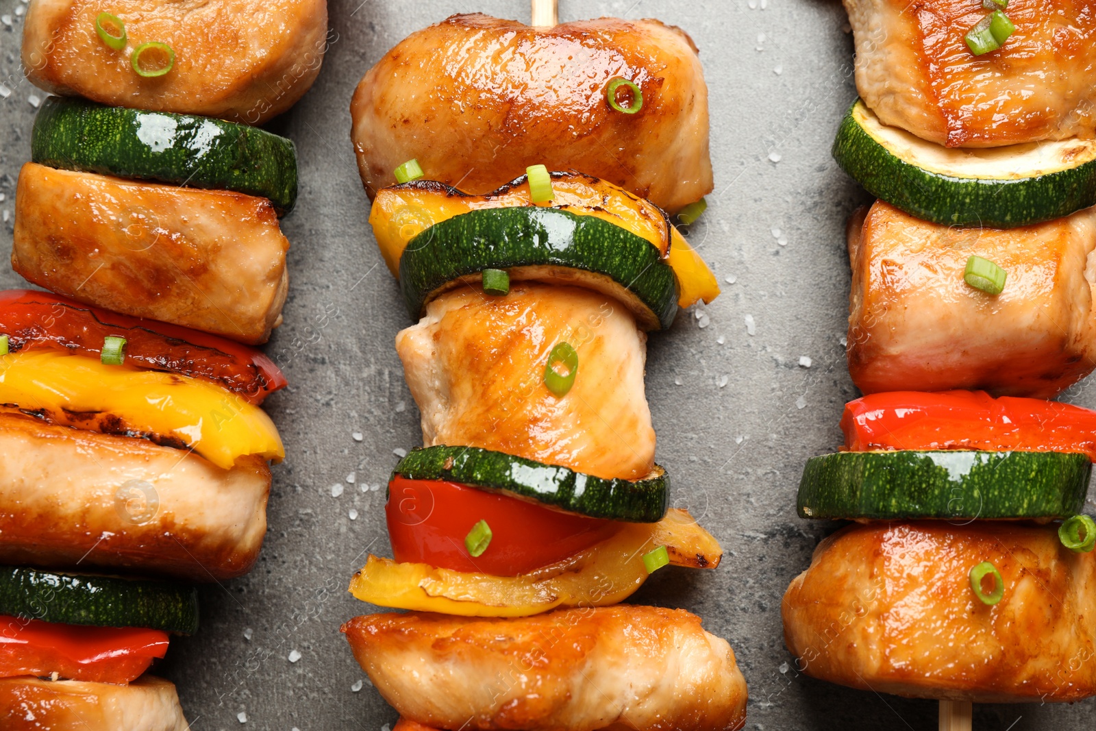Photo of Delicious chicken shish kebabs with vegetables and salt on grey table, flat lay