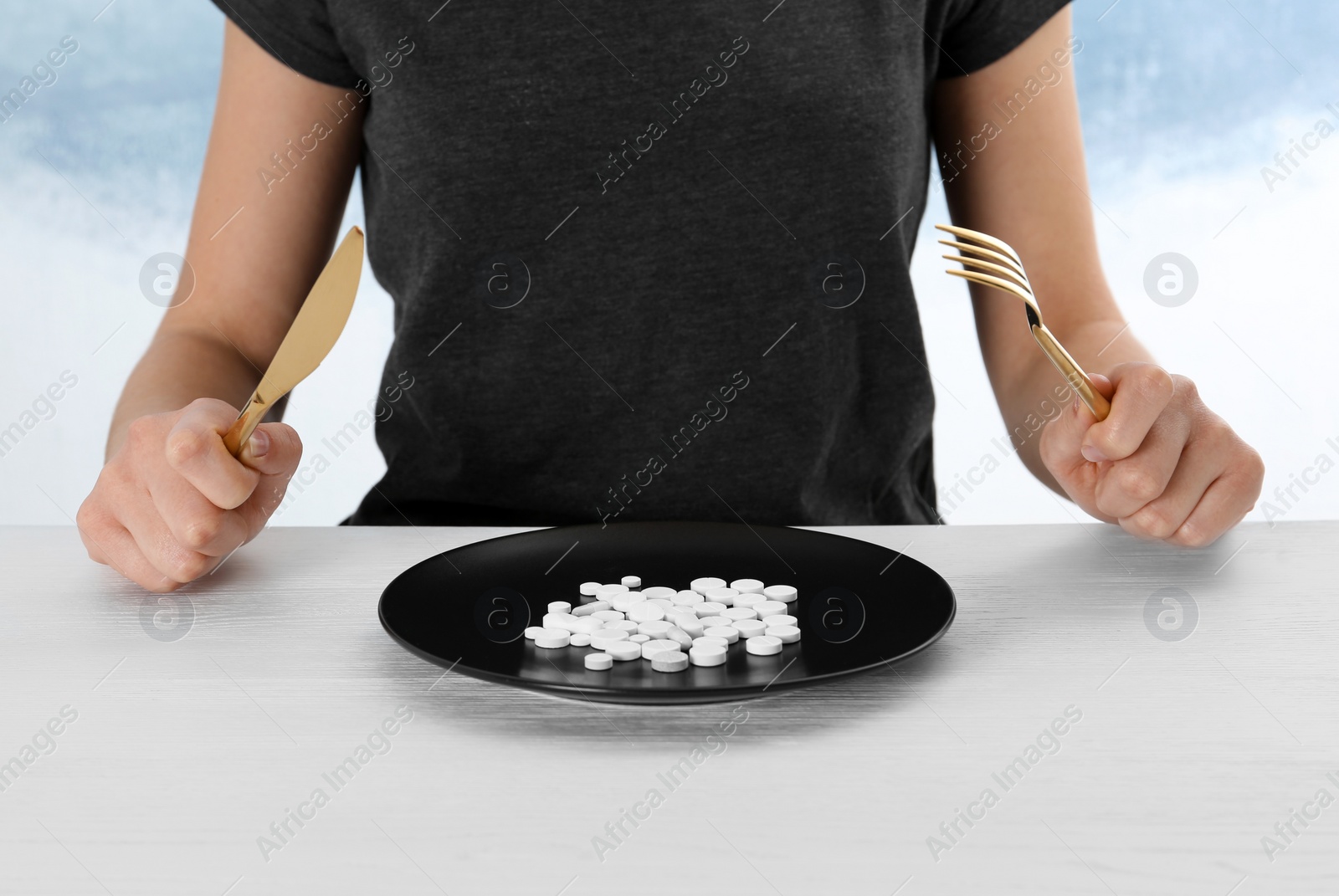 Photo of Woman sitting at table with cutlery and plate of weight loss pills, closeup