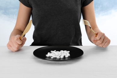 Woman sitting at table with cutlery and plate of weight loss pills, closeup