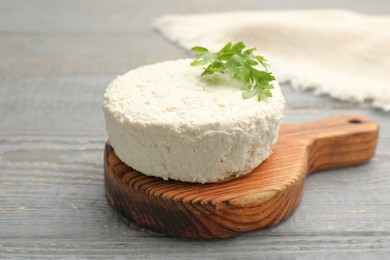 Photo of Delicious fresh cottage cheese with parsley on grey wooden table, closeup