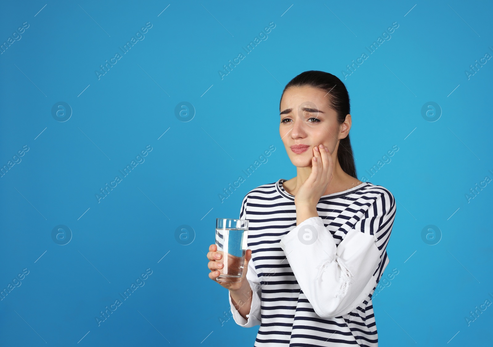 Photo of Emotional young woman with sensitive teeth and glass of water on color background. Space for text