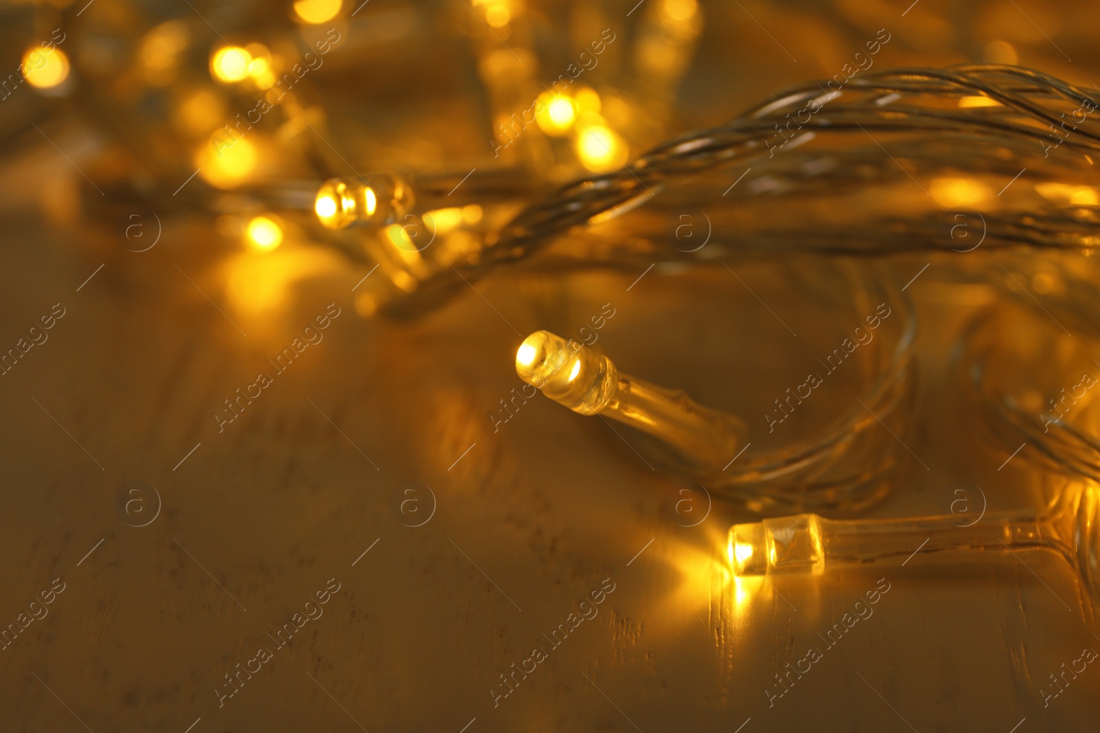 Photo of Glowing Christmas lights on white wooden background, closeup