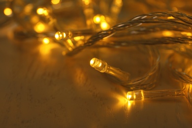 Photo of Glowing Christmas lights on white wooden background, closeup