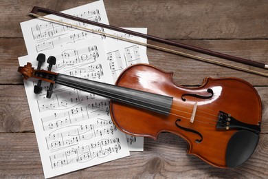 Violin, bow and music sheets on wooden table, top view