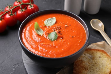 Photo of Delicious tomato cream soup served on black textured table, closeup
