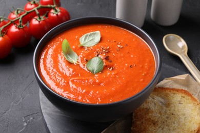 Delicious tomato cream soup served on black textured table, closeup