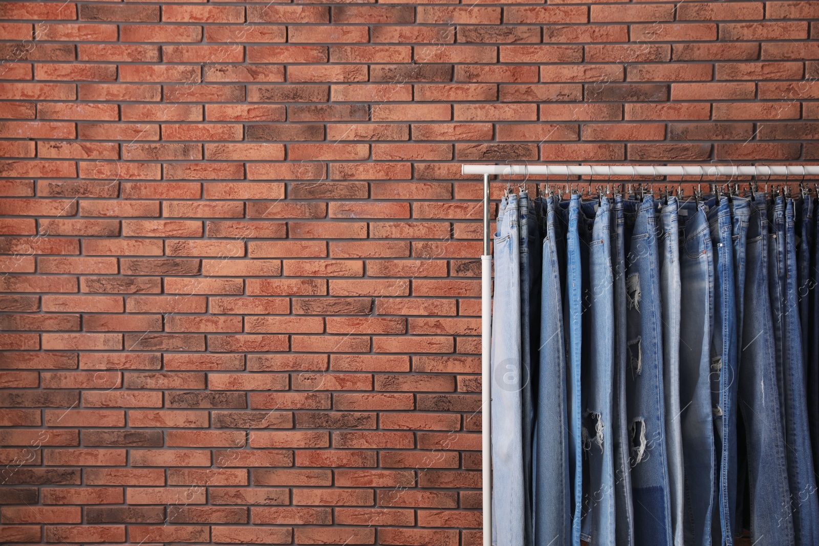 Photo of Rack with stylish jeans near brick wall. Space for text