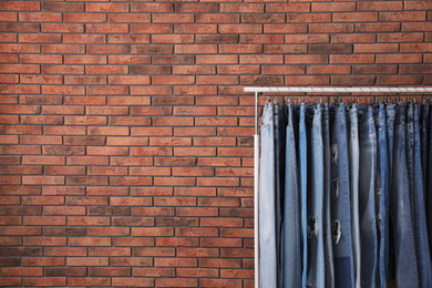 Photo of Rack with stylish jeans near brick wall. Space for text