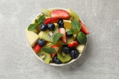 Photo of Tasty fruit salad in bowl on gray textured table, top view