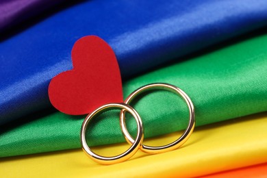 Photo of Wedding rings and heart on rainbow LGBT flag, closeup