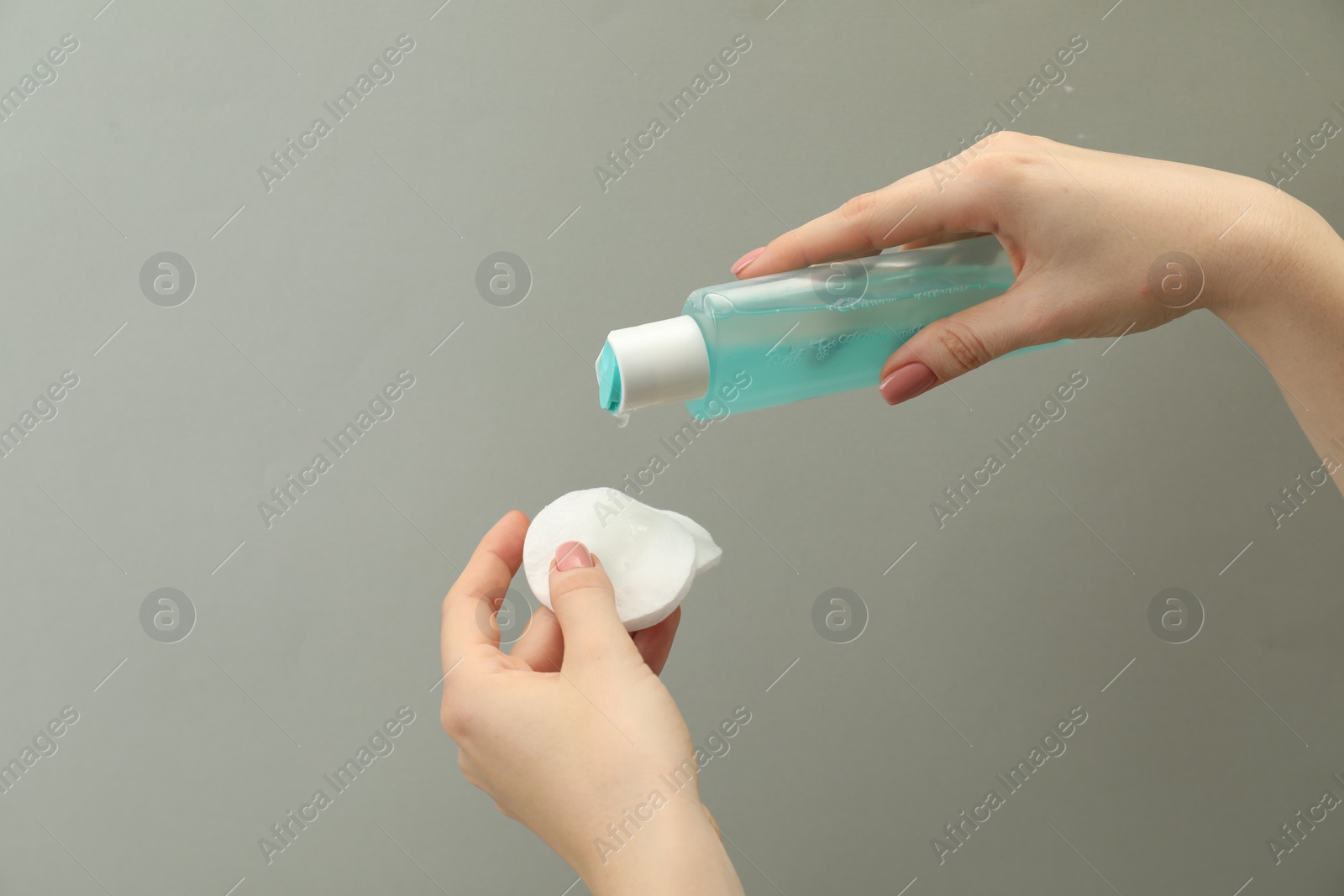 Photo of Woman pouring makeup remover onto cotton pads on light grey background, closeup