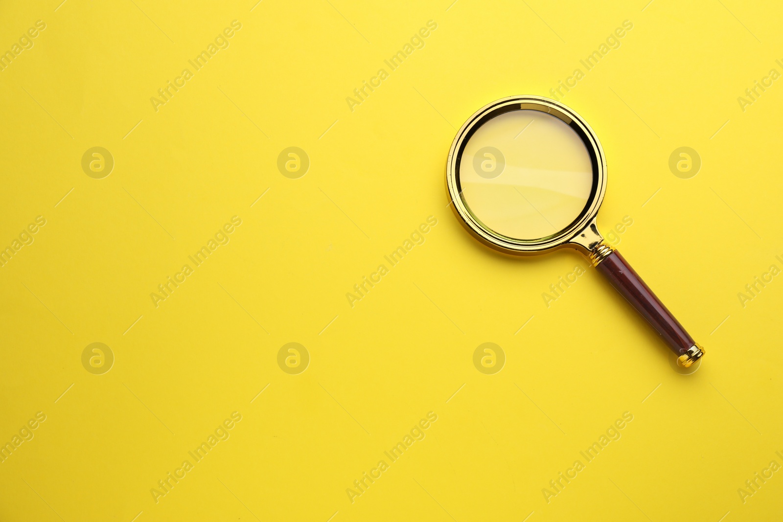 Photo of Magnifying glass on yellow background, top view. Space for text