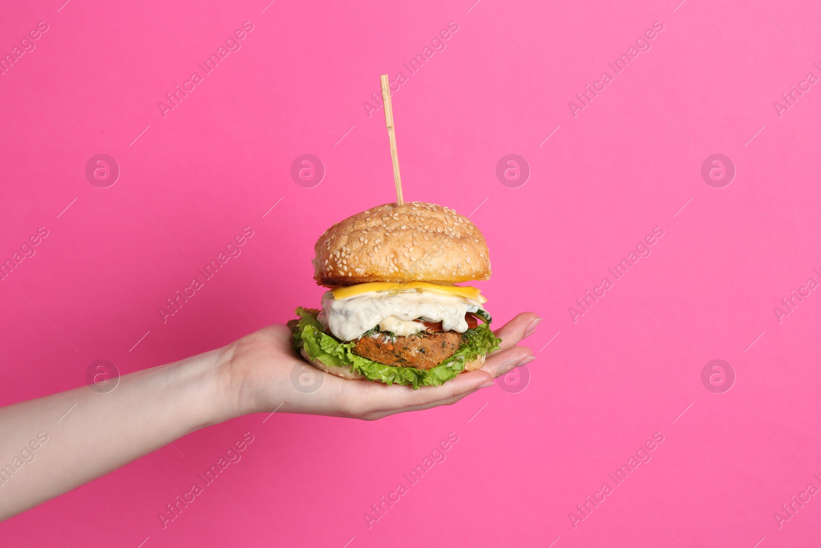 Photo of Woman holding delicious vegetarian burger on pink background, closeup