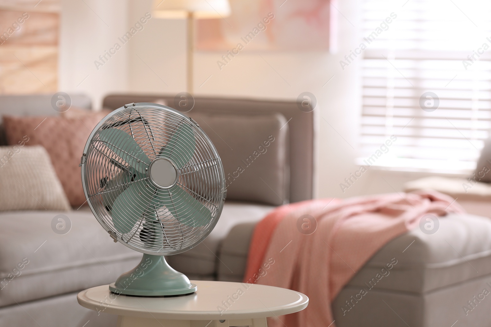 Photo of Modern electric fan on white table in living room. Space for text