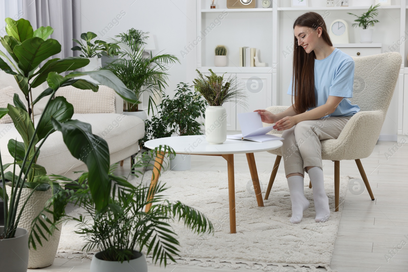 Photo of Beautiful young woman with book at table in room with green houseplants