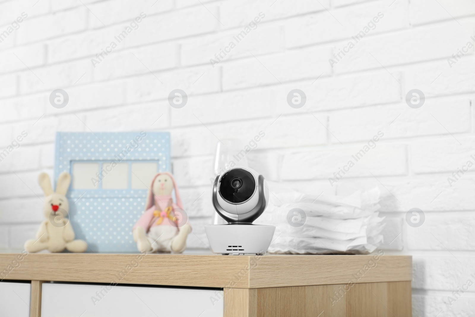 Photo of Baby camera and accessories on chest of drawers near white brick wall. Video nanny