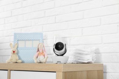 Photo of Baby camera and accessories on chest of drawers near white brick wall. Video nanny