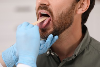 Doctor examining man`s oral cavity with tongue depressor on blurred background, closeup