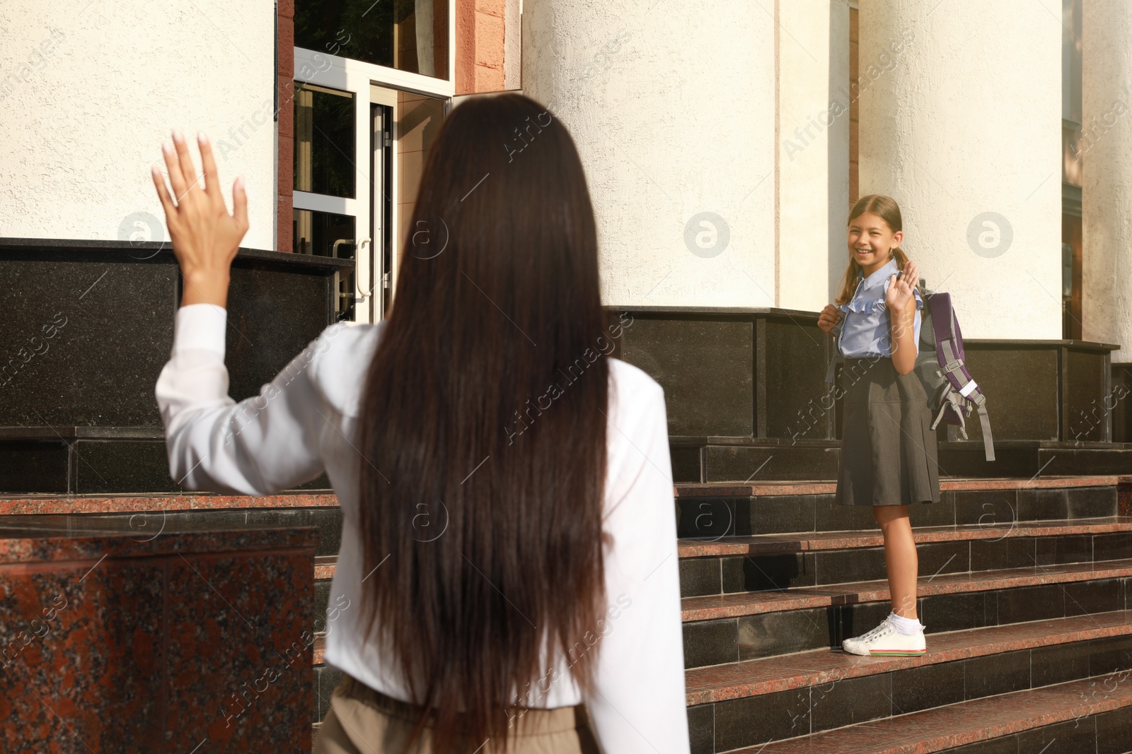 Photo of Mother waving goodbye to her daughter near school entrance