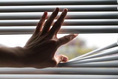 Photo of Man separating slats of white blinds indoors, closeup